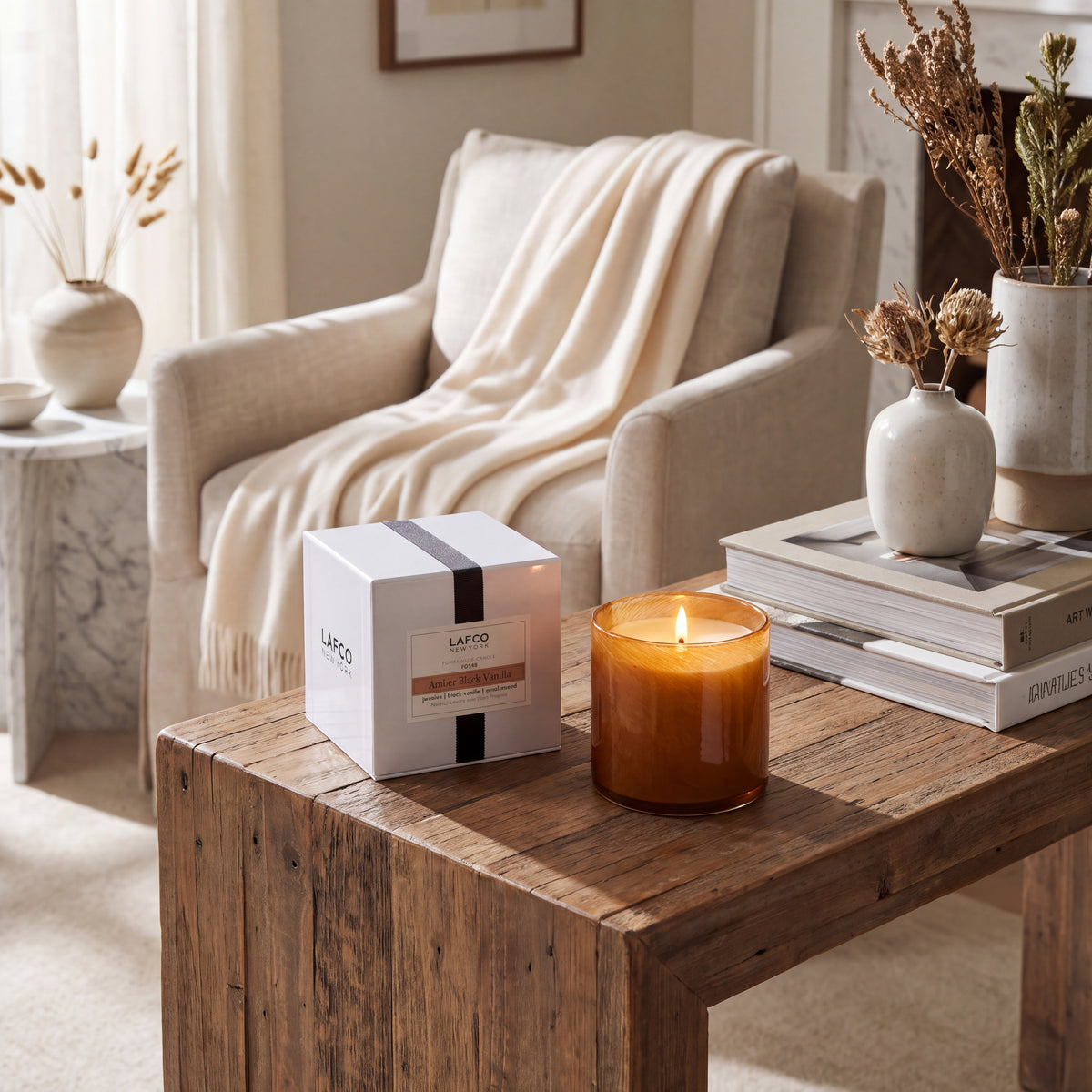 Cozy living room with a rustic wood coffee table, LAFCO candle, neutral armchair, and minimalist decor in a warm, modern style.