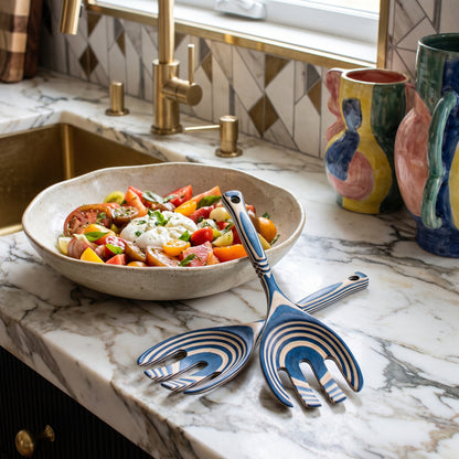 12 Blue Pakka Salad Claws displayed on a marble kitchen counter next to a fresh tomato and burrata salad bowl.
