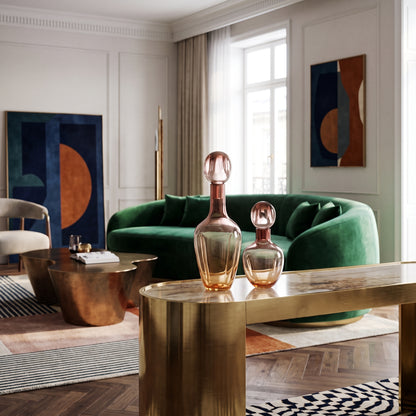 Modern living room with a green velvet curved sofa, brass coffee table, and elegant glass decanters on a gold console.