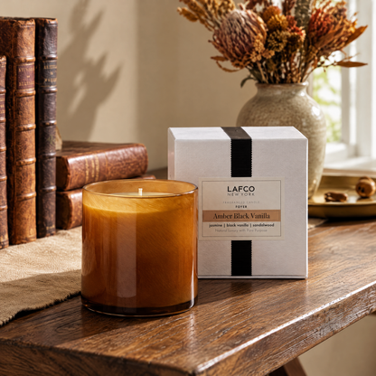 A LAFCO New York Amber Black Vanilla candle and box on a rustic wooden table with vintage books and dried flowers.