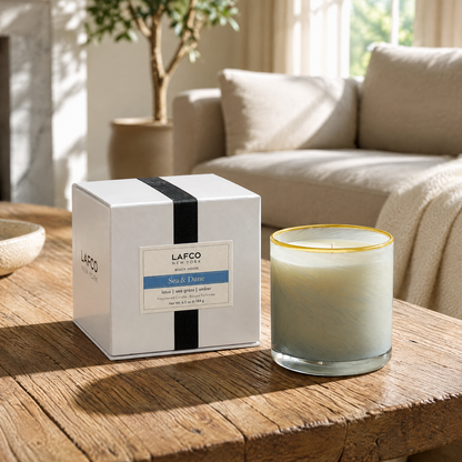 Lafco New York Sea & Dune candle set on a rustic wooden coffee table in a bright, modern minimalist living room.